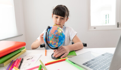 Asia kid girl funny with use magnifying glass to earth model in living room at home