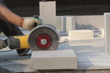 Hands of worker with electric grinder trims paving slabs on the construction site. Concept of...