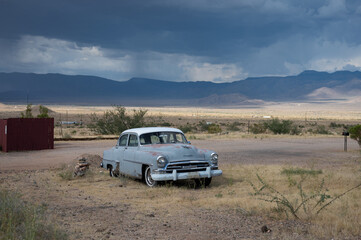 Old blue gray 1954 car with white top abandoned on desert road