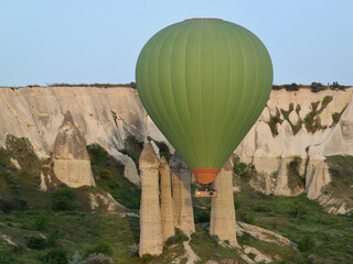 Green hot air balloon with the rock formations in the background flying over Cappadocia Turkey
