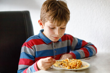 Cute healthy schoolkid boy eats pasta noodles sitting in school or nursery cafe. Happy child eating healthy organic and vegan food in restaurant or at home. Childhood, health concept