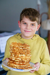 Portrait of happy school kid boy holding fresh baked waffles. Smiling hungry child with sweet biscuit wafer. Sweet sugar belgian waffles.