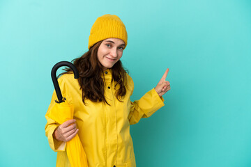 Young caucasian man holding an umbrella isolated on blue background pointing back