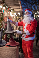 Portrait von einem verkleideten Weihnachtsmann, der auf einem Weihnachtsmarkt von Lichtern umgeben ist