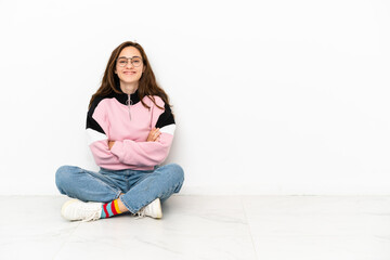 Young caucasian woman sitting on the floor isolated on white background keeping the arms crossed in...