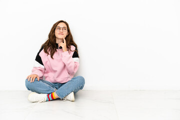 Young caucasian woman sitting on the floor isolated on white background thinking an idea while looking up