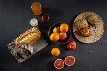 Bread, croissants, rolls, homemade yogurt, marmalade and honey jars, oranges, apples and sliced ​​grapefruit on the table in a rustic wooden bowl and wooden plate