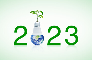 2023 text and earth globe inside led light bulb with fresh green tree leaves on soil, Happy new...