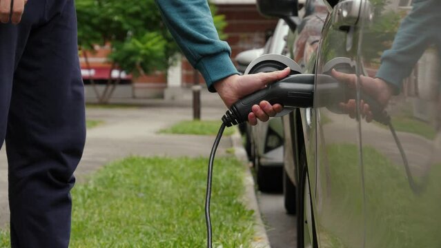 Unrecognizable man disconnects charging cable into electric car. Male hand unplugs power connector into EV car