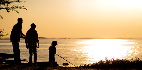 father and sons fishing in the river sunset background. Silhouette of man and two boys fishing at...