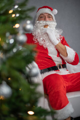 Portrait von einem verkleideten Weihnachtsmann, der auf ein Chaiselongue neben einem Weihnachtsbaum sitzt