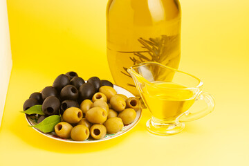 Jug with olive oil, green and black olives on yellow background.