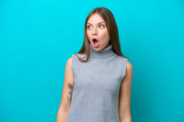 Young Lithuanian woman isolated on blue background doing surprise gesture while looking to the side