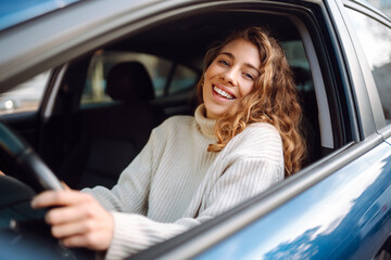 Pretty woman driver smiling to you from the  car. Automobile Journey, traveling, lifestyle concept. Car sharing.