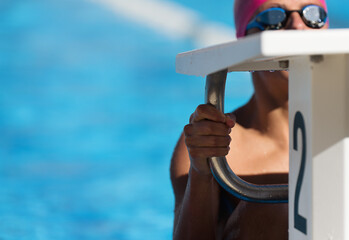 Female swimmer holding onto starting block preparing to swim backstroke. Focus on hand