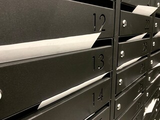 close-up of bills in metal mailboxes with apartment numbers in an apartment building. Utility bills, tax notices, payment documents and white sheets of mail notices in mailboxes close-up.