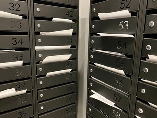 close-up of bills in metal mailboxes with apartment numbers in an apartment building. Utility bills, tax notices, payment documents and white sheets of mail notices in mailboxes close-up.