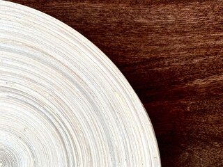 close-up of a part of a light wooden plate on a dark wooden tabletop. wooden plate with concentric texture on a wooden table.