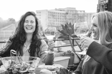 Happy friends celebrating cheering with wine outdoor in winter time at patio restaurant - Focus on left girl face - Black and white editing