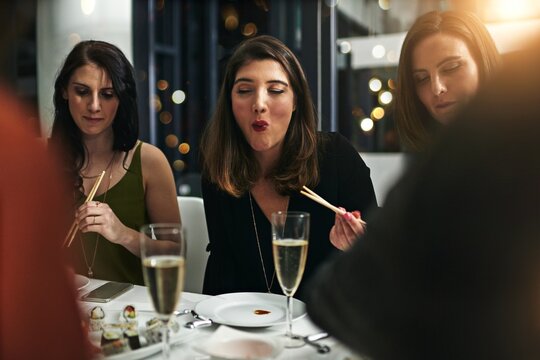 Friends, dinner party and at a restaurant for celebration, happiness or eating. Young people, women and champagne for event, conversation and alcohol for social gathering, sushi and speaking to relax