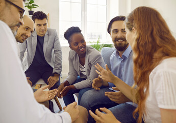 Several multiracial people sitting together and talking. Group of happy diverse coworkers and friends sharing news. Team of mixed race employees sitting on couch and telling what happened in office