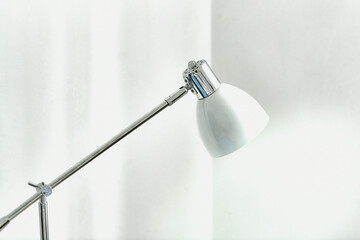 Fototapeta Chromowana lampa, lampka na stolik z białym kloszem na tle białych ścian rzucająca snop światła. obraz