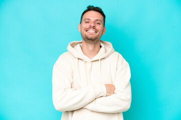 Young caucasian handsome man isolated on blue background keeping the arms crossed in frontal...