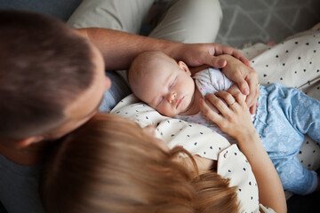 Portrait of sleeping newborn baby in arms of parents, mom and dad, top view. Close up family with...