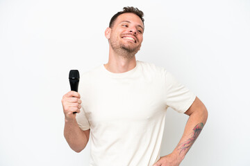 Young caucasian singer man picking up a microphone isolated on white background posing with arms at...