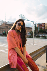 Young adult model with cool glasses and outfit posing for camera with a basketball field in the background