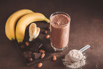 Chocolate milkshake smoothie with banana, protein powder and nuts on dark background