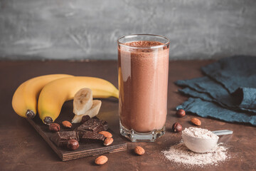 Chocolate milkshake smoothie with banana, protein powder and nuts on dark background