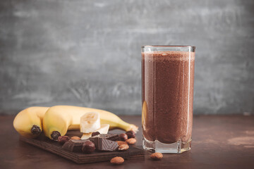 Chocolate milkshake smoothie with banana, protein and nuts on dark background