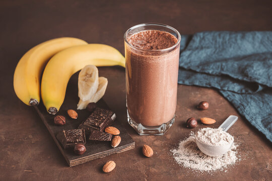 Chocolate milkshake smoothie with banana, protein powder and nuts on dark background