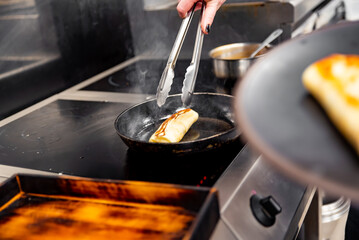 chef hand cooking Thin pancakes crepe rolls with ground meat in pan at a restaurant kitchen