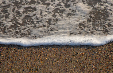 a close-up of a small wave with foam on the shore sand
