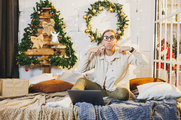 Happy smiling woman in glasses lies on the bed on the background of Christmas decorations. The woman is happy with the Christmas holidays. New Year's atmosphere at home.