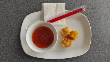 Fried dumpling on the white plate with sweet chili sauce on the bowl, tissue and chopsticks