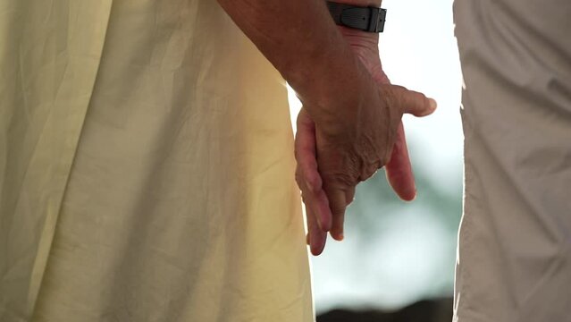 Close up of senior married couple joining hands together with sunlight flare shining in background. Beautiful moment between older people hands held in support