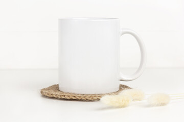 Mockup of white mug on table with jute coaster and dried flowers, neutral color. Blank coffee cup mug mock up in Boho style. - obrazy, fototapety, plakaty