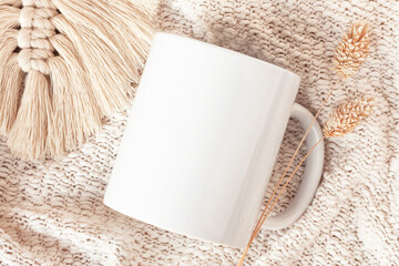 Mockup of white mug on knitted plaid with macrame decor and dried flowers, neutral color. Blank...