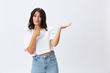 Woman in white t-shirt on white background brunette hands up gestures and signals poses in jeans emotion, lifestyle smiles, copy space