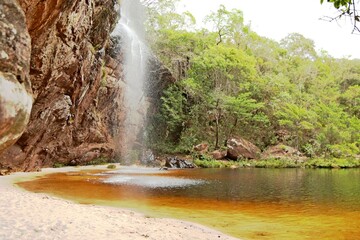 Waterfall through rocks in the middle of the forest in Minas Gerais. Small trees, fresh water falling forming a small lake.