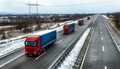 Convoy of Red Transportation Trucks on a Highway in a snowy winter landscape. Business Transportation And Trucking Industry.