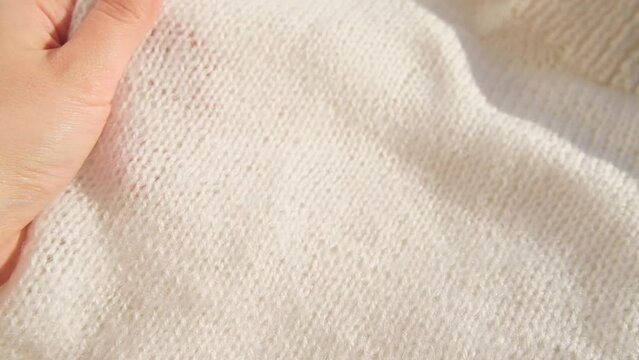 Close up hand stroking over the surface knitted soft wool cloth or warm fluffy sweater. Handcraft knitting woolen fabric.