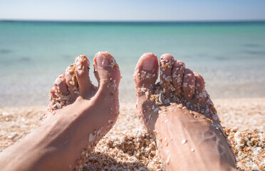 Women's legs in shells on the background of the Azure Sea