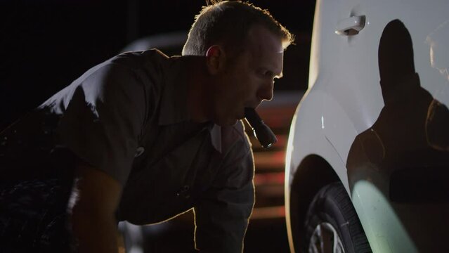 Roadside mechanic holding flashlight in mouth jacking up car at night / Nephi, Utah, United States