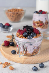 Chocolate granola with berries, chia seeds and natural yogurt in two jars on gray background