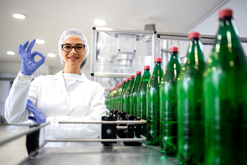 Female technologist holding okay sign and approving production in beverage bottling factory.