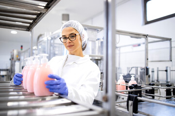 Female production line worker in white sterile uniform and hairnet working for pharmaceutical company and producing liquid soap cleaning chemicals.